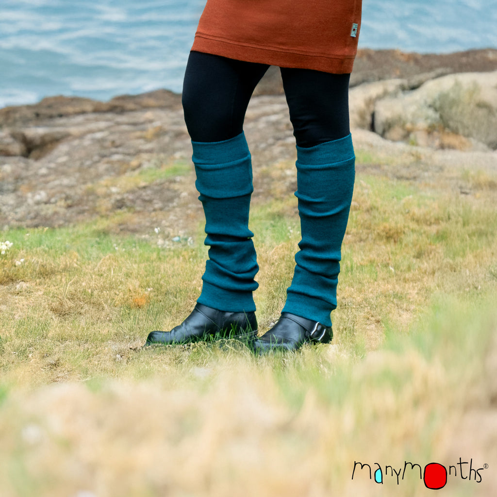 woman wearing merino wool leg warmers in teal by the beach in black boots and black leggings